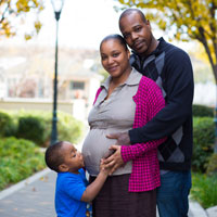 Photo of a black family in a park with the dad wrapping his arms around his pregnant wife and the son kissing his mom's belly Photo of a black family in a park with the dad wrapping his arms around his pregnant wife and the son kissing his mom's belly